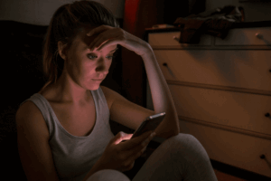 Woman sits on the floor, looking at her phone with a concerned expression.