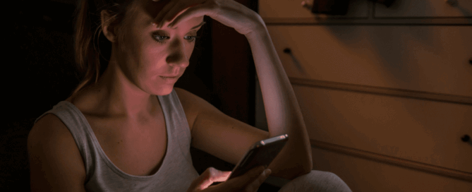 Woman sits on the floor, looking at her phone with a concerned expression.