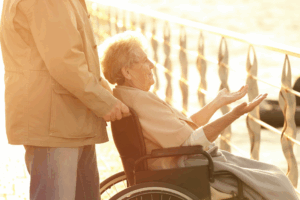 Elderly woman sitting in a wheelchair, with her hands raised.