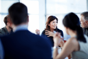 A woman is engaged in a discussion during a meeting, gesturing as she speaks.