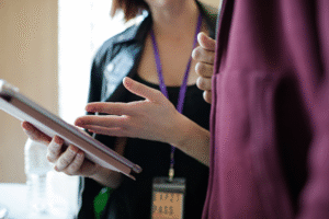 A person's hand holding a tablet, explaining something with another person.