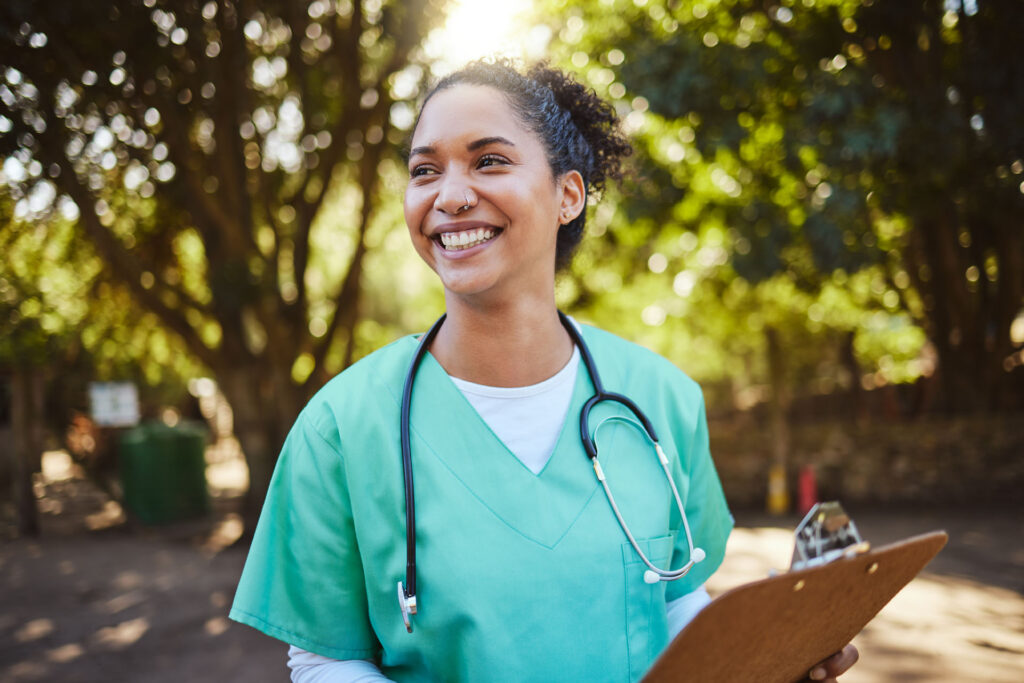 A healthcare professional wearing green scrubs and a stethoscope around her neck is holding a clipboard.