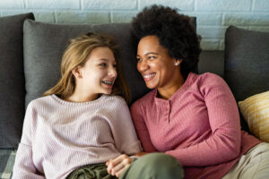 Two women sitting closely together on a couch, smiling and looking at each other.
