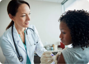 A healthcare professional in a white coat with a stethoscope administers a vaccination to a young girl.