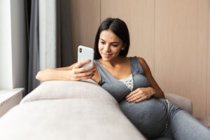 Pregnant woman sitting on sofa using mobile phone.