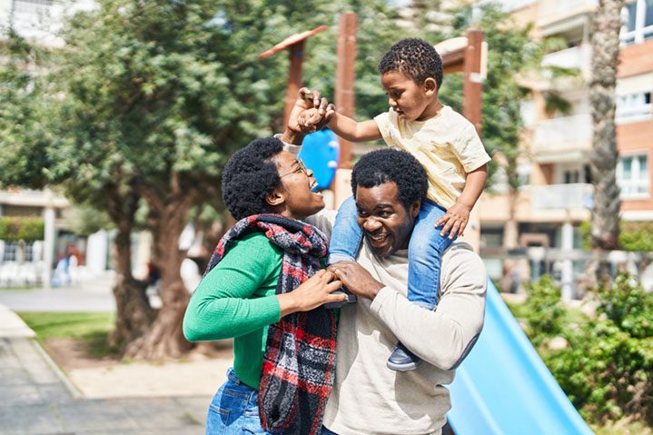 African american family holding boy on shoulders at playground.