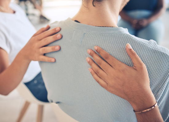 Mental_Health Comforting hands on a woman's back in group therapy session