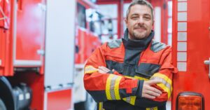 A firefighter in uniform standing with his arms crossed, smiling confidently.