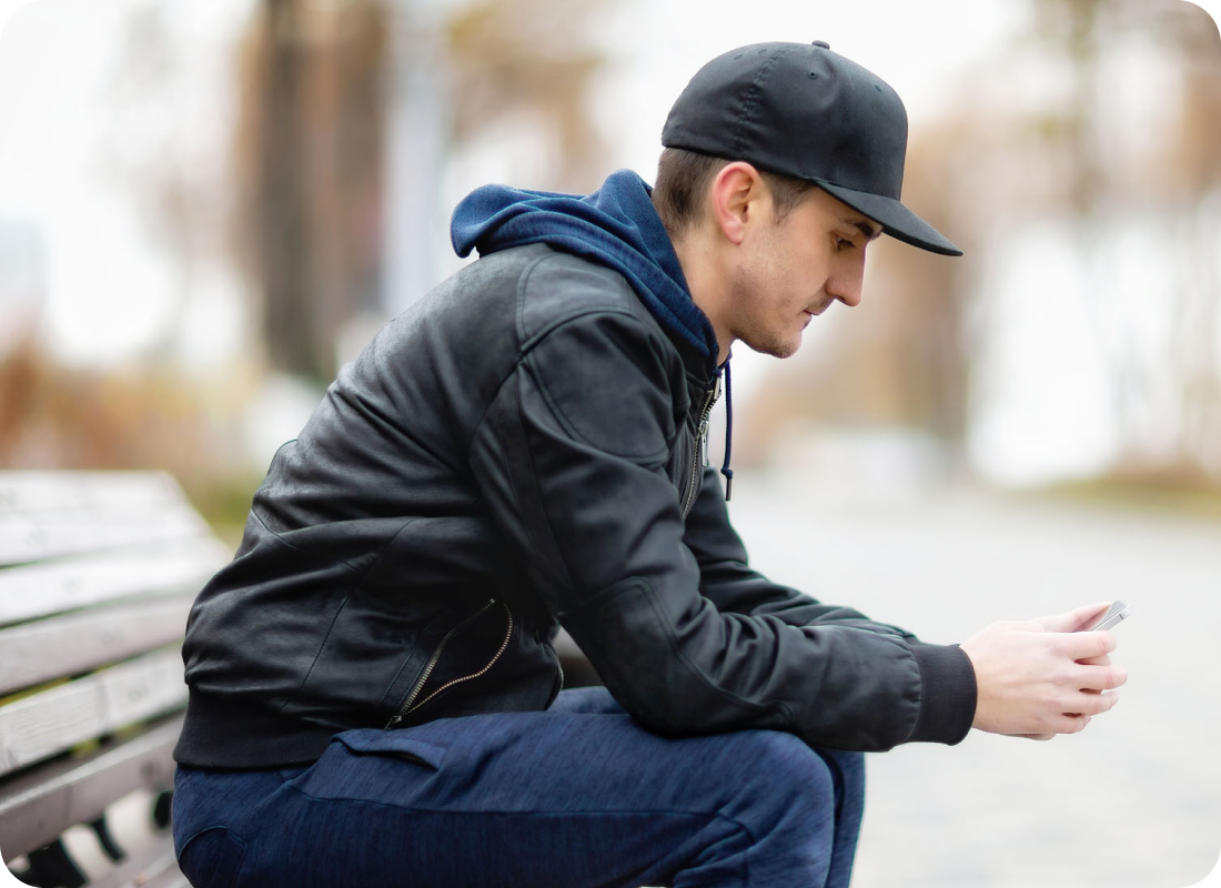 A young man sitting on a bench outdoors.