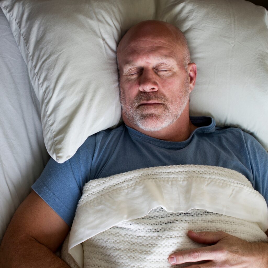 A man lies asleep on a bed.