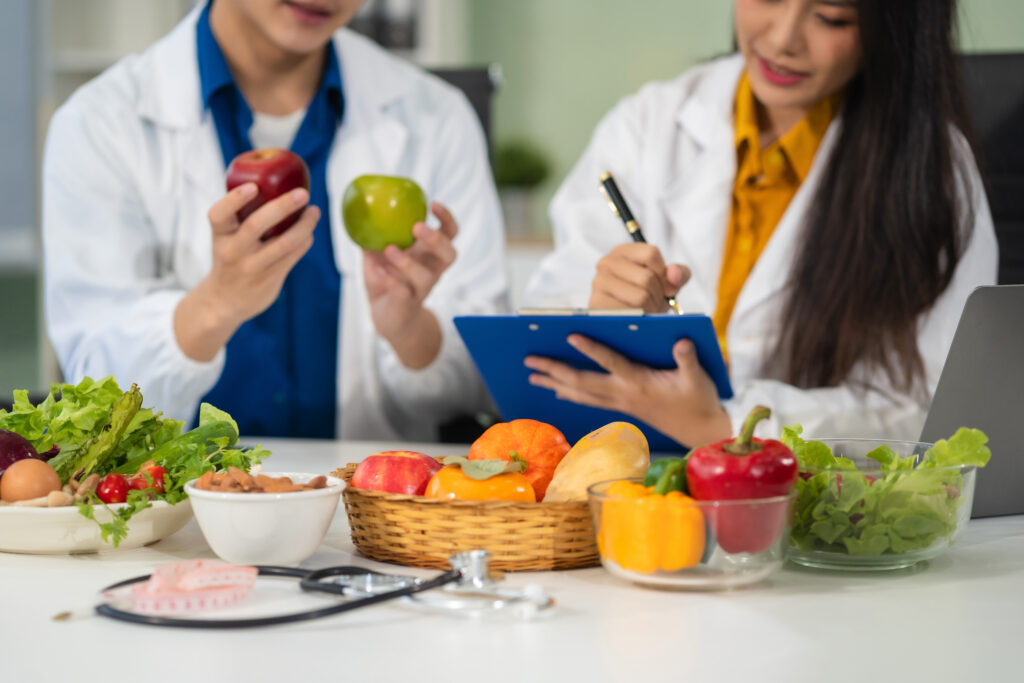 Experts discussing nutrition, psychiatry, and health research. Two professionals in lab coats examine apples and record notes.